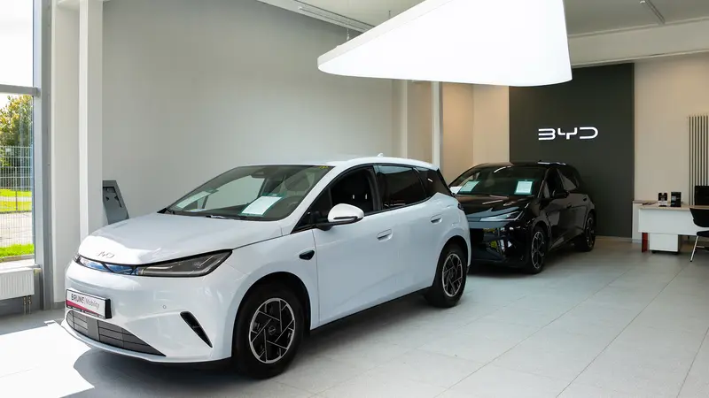 Zwei moderne BYD-Elektroautos in unserem hellen Showroom, vorne ein weißes Modell, dahinter ein schwarzes Modell, mit BYD-Logo an der Wand