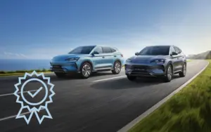 Zwei moderne BYD-Elektro-SUVs fahren nebeneinander auf einer Küstenstraße bei klarem Himmel.