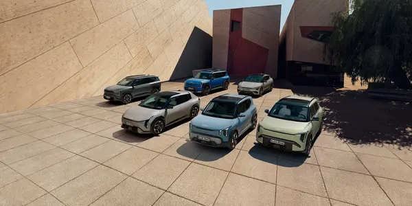 Kia EV Range in verschiedenen Farben auf einem großen gepflasterten Platz vor einem Gebäude mit schrägen Wänden und klaren geometrischen Formen