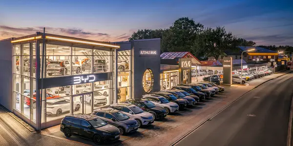 Beleuchtetes Autohaus in Bramsche mit BYD-und Kia-Logo und einer Reihe geparkter Autos entlang einer Straße bei Dämmerung